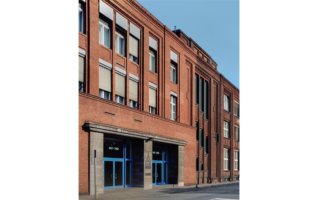 Backsteingebäude als Sitz der Firmenzentrale KHD-Konzerns an der Deutz-Mülheimer Straße 147-149. Der Eingang ist 1938 als Überbauung einer ehemals ins Werksgelände hineinführenden Werksstraße entstanden (1996).