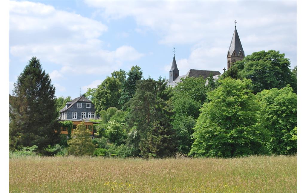 Kloster Saarn, wie es sich beim Blick aus der Ruhraue zeigt. Das Kloster liegt erhöht am Talhang und ist von altem Baumbestand umgeben (2015).