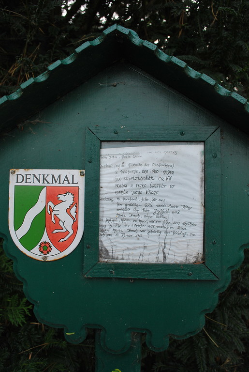 Die hölzerne Infotafel beschreibt das Wegekreuz am Mockenhof und übersetzt die Inschrift.