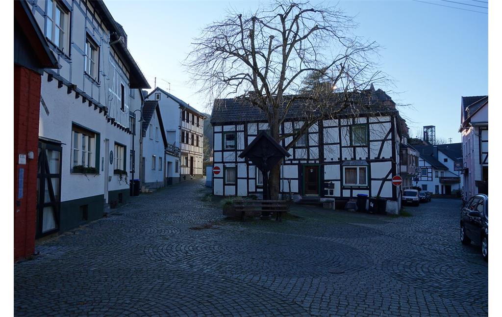 Die Straße "Am Giebel" im historischen Kern von Heimbach teilt sich an einem kleinen Platz, in dessen Mitte ein hölzernes, bedachtes Wegekreuz steht (2020).