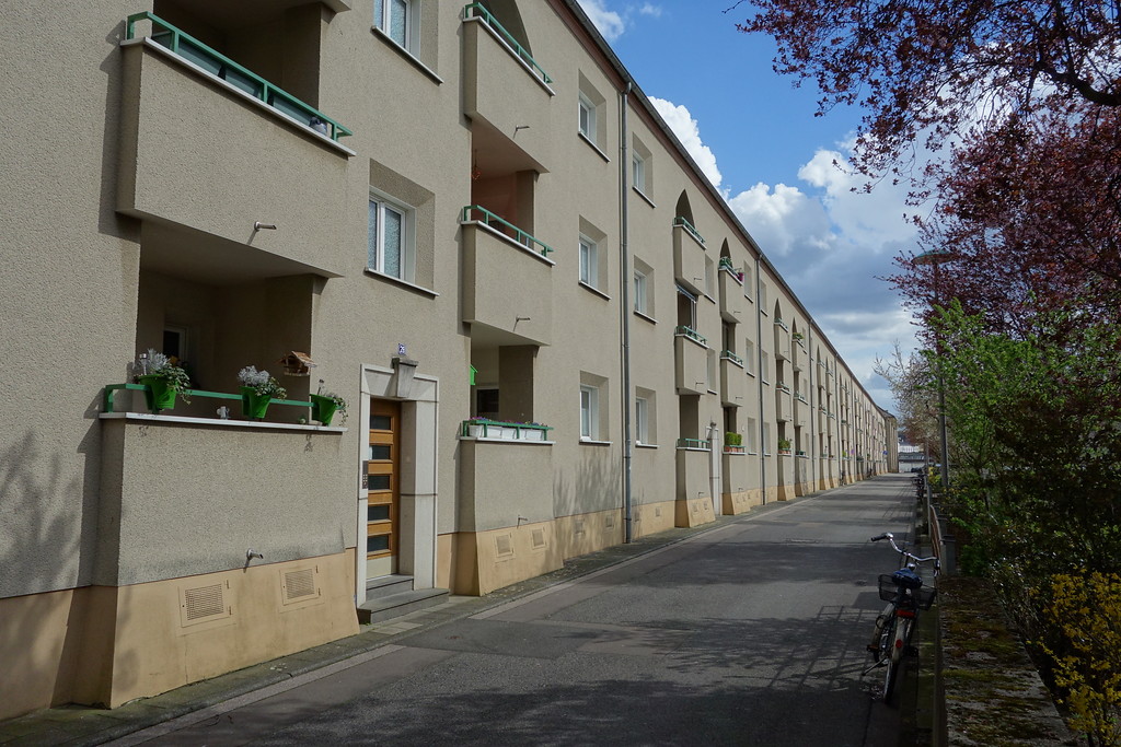 Köln-Mauenheim: Für die Siedlung "Grüner Hof" kennzeichnend ist eine dreigeschossige Blockrandbebauung aus Mehrfamilien-Reihenhäusern, die um große, begrünte Innenhöfe angeordnet sind. Die Fassaden sind sparsam gegliedert durch Balkone (2016).