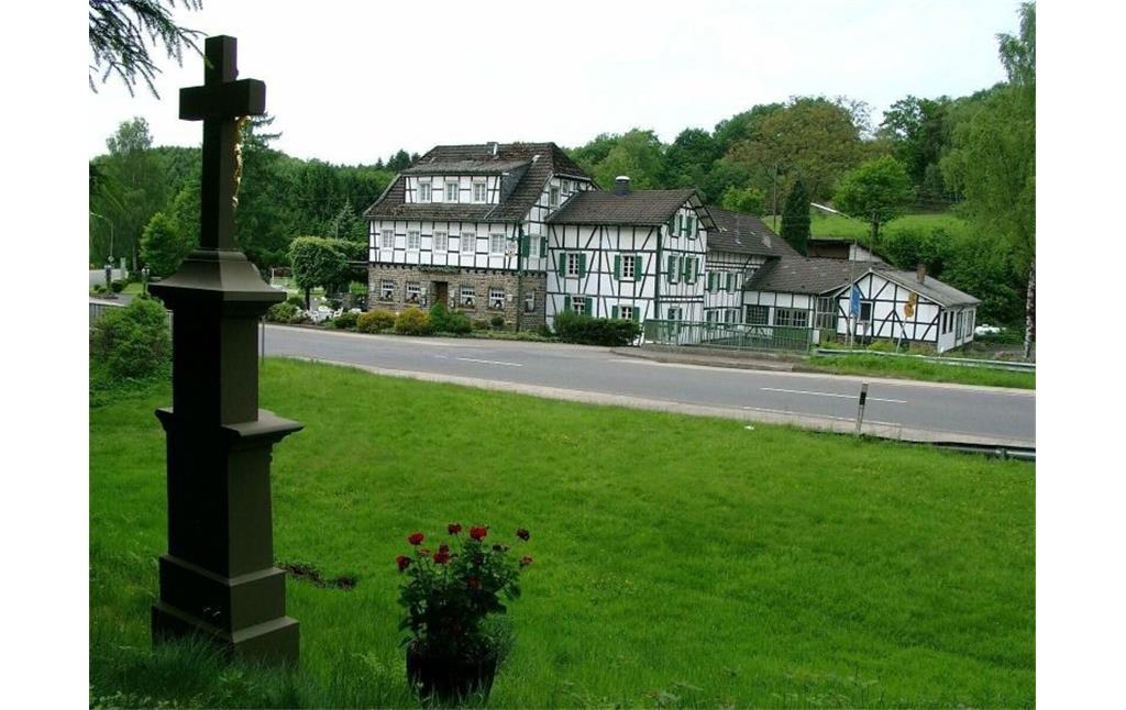 Blick auf die Fischermühle am Naafbach von der Straßenseite aus (2003). Im Vordergrund steht ein Wegekreuz.