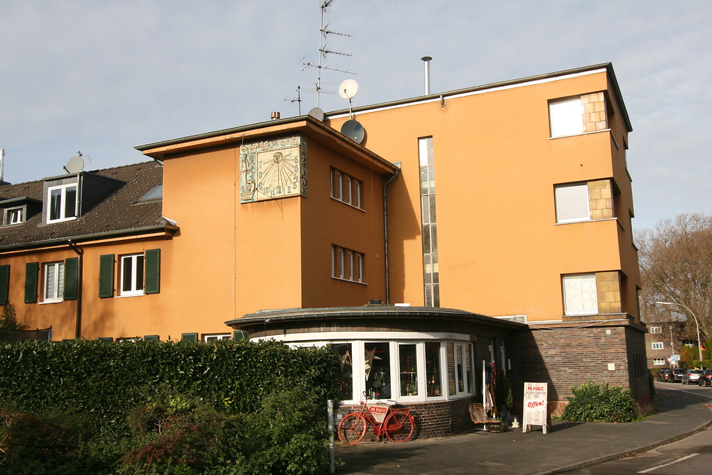 Gelb verputztes Mehrfamilienhaus mit pavillonartigem Anbau und Sonnenuhr aus Keramik in der Keimesstraße Ecke Hasenweide (2021)