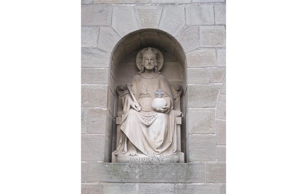 In der Hofmauer eines Hauses in Bürvenich sitzt eine steinerne Königsfigur mit Krone, Reichsapfel und Zepter auf dem Thron. Im Sockel eingraviert steht: "UNSEREM KÖNIG".(2014)