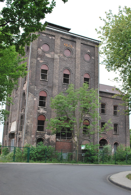 Der denkmalgeschützte Malakoffturm über Schacht I der Zeche Rheinpreußen ist mit einem Teil der Schachthalle erhalten geblieben. Die Giebelinschrift verweist auf das Jahr 1879, als die Förderung begann (2015).