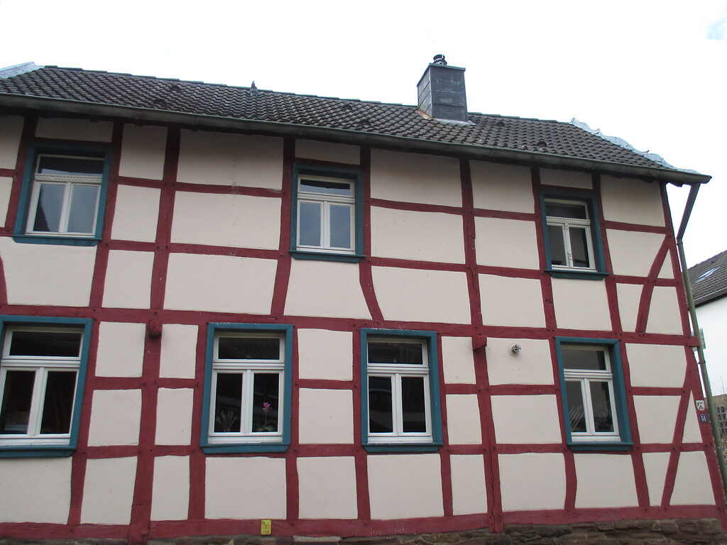 Haus in Fachwerkbauweise auf Bruchsteinsockel, die Balken sind rot und die Fenstereinfassungen blau gestrichen (2015)