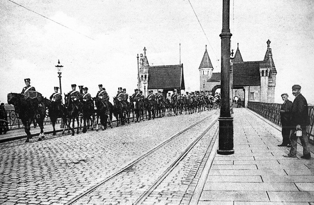 Undatierte Aufnahme der 1898 eingeweihten Alten Bonner Rheinbrücke, mit einem Trupp Husaren. Die Gleise der elektrischen Straßenbahn, die erst seit 1902 über den Rhein nach Beuel fuhr, lassen auf die Zeit danach schließen.