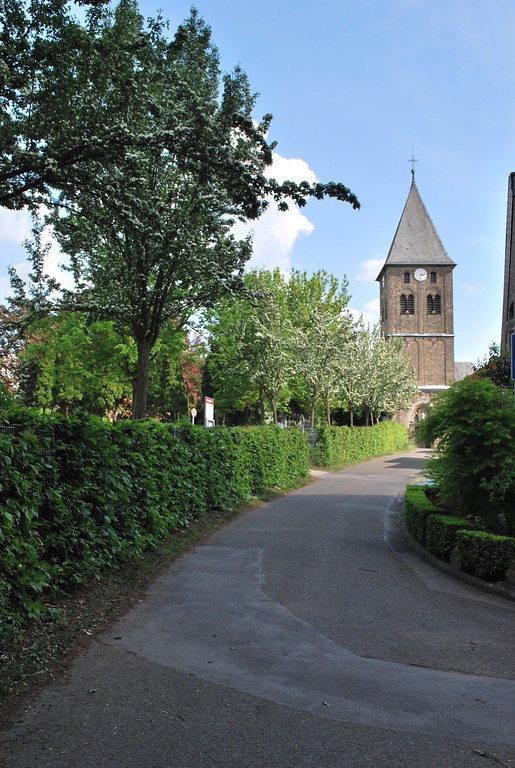 Blick durch die Straße "An der Dränk" auf die romanische St. Martinus-Kirche in Esch. Links im Bild zu sehen ist der durch eine Hecke eingefasste Friedhof (2014).