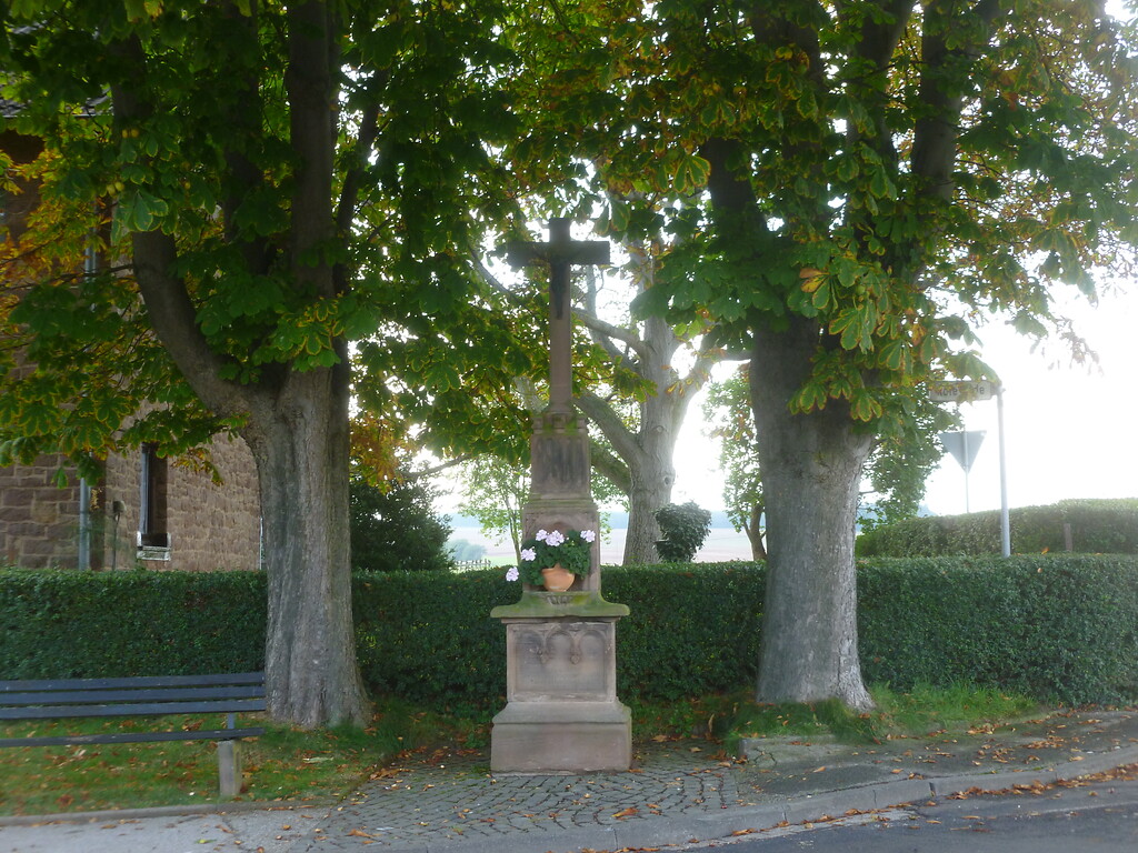 Dieses verzierte Wegekreuz aus Sandstein am östlichen Ortseingang von Glehn wird von zwei mächtigen Kastanienbäumen flankiert. (2014)