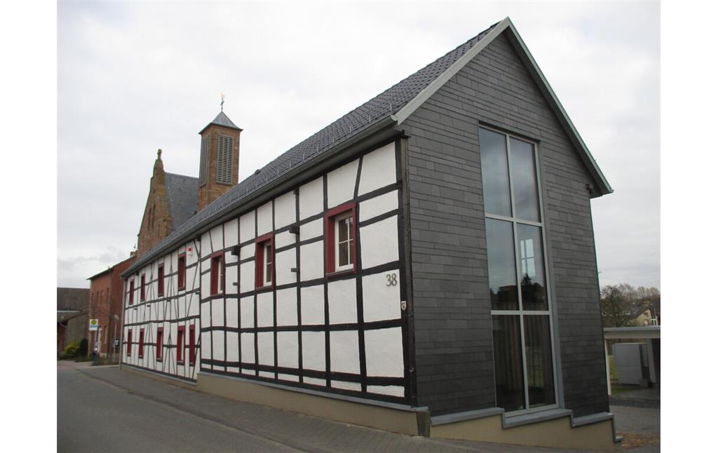 Ehemaliges Wohn-Stall-Haus in Fachwerkbauweise mit modernisiertem Giebel, im Hintergrund die Pfarrkirche St. Gereon (2015)