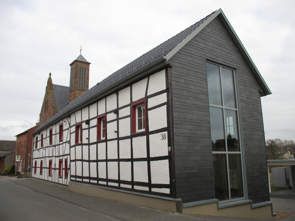 Ehemaliges Wohn-Stall-Haus in Fachwerkbauweise mit modernisiertem Giebel, im Hintergrund die Pfarrkirche St. Gereon (2015)