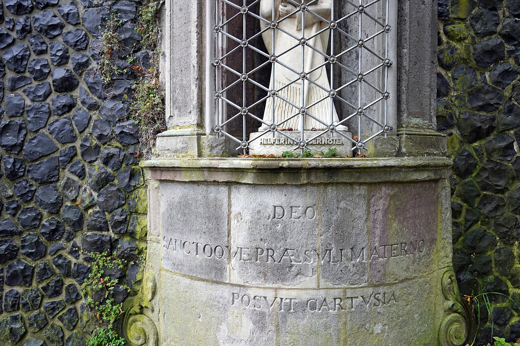 Inschrift am "Helfer in Wassernöten" am Rodenkirchener Leinpfad direkt am Rhein in Köln-Rodenkirchen (2021), die Skulptur stellt den als Heiligen Maternus verehrten ersten Bischof von Köln dar.