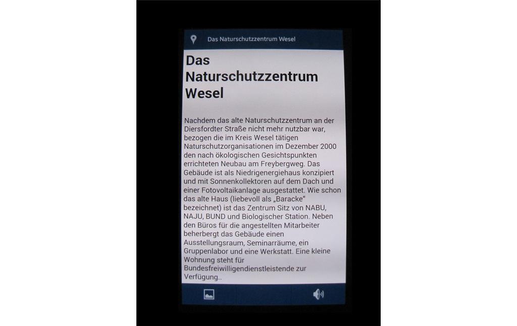 Bildschirm-Foto eines Mobilgerätes von der Anwendungssoftware "App in die Natur!". Es ist den Naturlehrpfad durch das Naturschutzgebiet Weseler Aue und zeigt den Text für den Informationspunkt "Das Naturschutzzentrum Wesel" (2014).