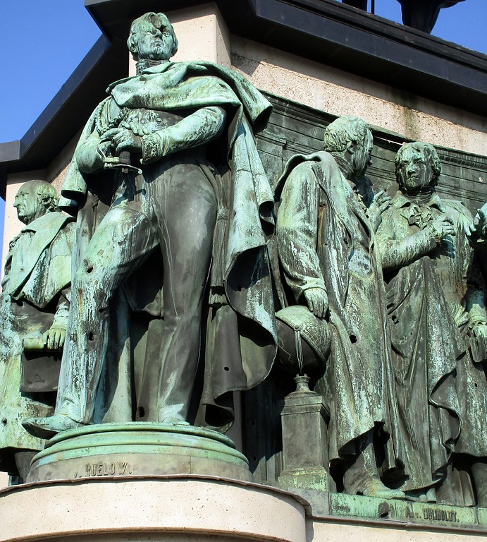 Sockelfiguren auf dem Reiterstandbild auf dem Kölner Heumarkt: Reichsfreiherr vom und zum Stein, Graf von Bülow, Alexander von Humboldt und Marcus von Niebuhr (2018).