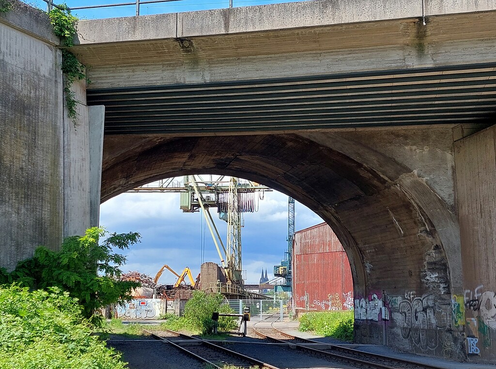 Blick durch einen Bogen der Südbrücke im rechtsrheinischen Köln-Poll auf Gleise der Hafenbahn und den Schrottplatz am südlichen Ende des Deutzer Hafenbeckens (2021).