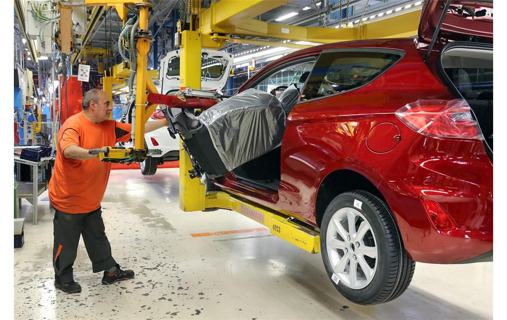 Fließbandproduktion im Ford-Autowerk in Köln-Niehl (2017), der Einbau des Fahrersitzes in einen Ford Fiesta wird durch eine hydraulische Hubvorrichtung unterstützt.
