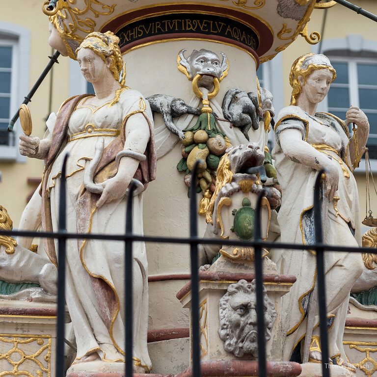 Detail am Petrusbrunnen auf dem Hauptmarkt in Trier (2022): Vier Statuen am Sockel stellen die Kardinaltugenden dar, links die Sapientia (Weisheit) und rechts die Justitia (Gerechtigkeit), hinter deren Rücken am Brunnenstock vollführen Affen allerlei Untugenden.