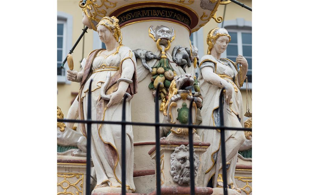 Detail am Petrusbrunnen auf dem Hauptmarkt in Trier (2022): Vier Statuen am Sockel stellen die Kardinaltugenden dar, links die Sapientia (Weisheit) und rechts die Justitia (Gerechtigkeit), hinter deren Rücken am Brunnenstock vollführen Affen allerlei Untugenden.