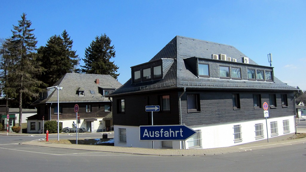 Historische Gebäude an der Einfahrt zum alten Fahrerlager am Nürburgring (2013). Vor dem hinteren Gebäude das 2002 errichtete Denkmal für den argentinischen Rennfahrer Juan Manuel Fangio.
