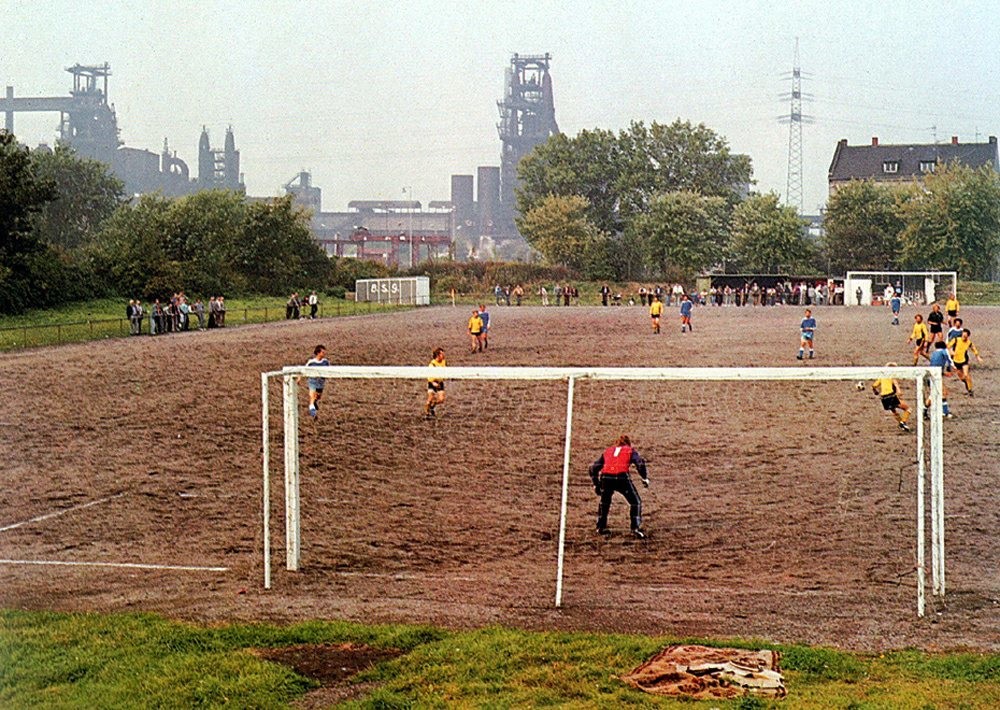 Ein Fußballspiel in Gelsenkirchen 1982, im Hintergrund sind Hochöfen der Zeche "Schalker Verein" zu sehen.
