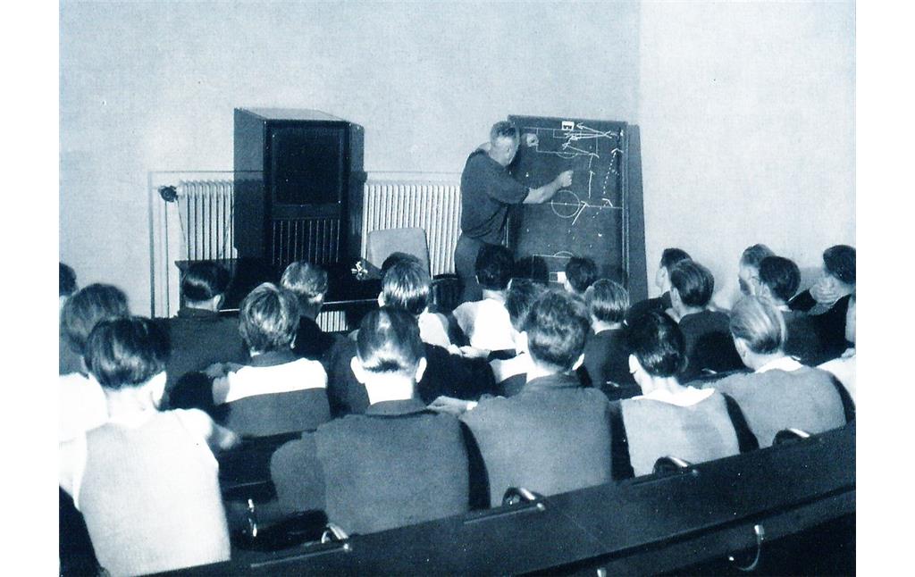 Ein Sportlehrer an der Taktiktafel, im Vordergrund die lauschenden Schüler (Aufnahme zwischen 1950 und 1955).
