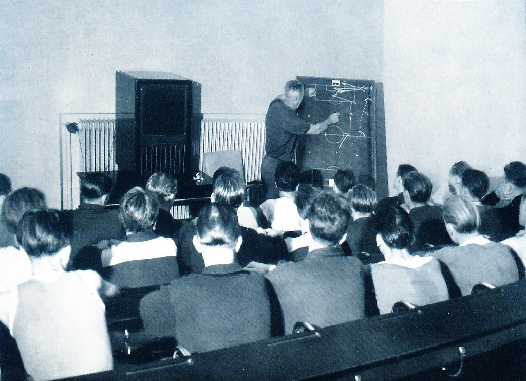 Ein Sportlehrer an der Taktiktafel, im Vordergrund die lauschenden Schüler (Aufnahme zwischen 1950 und 1955).
