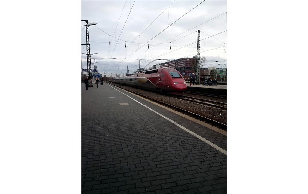 Ein durch den Bahnhof Köln Messe/Deutz fahrender Thalys-Hochgeschwindigkeitszug sowie Bahnsteige und Gleiskörper (2015).