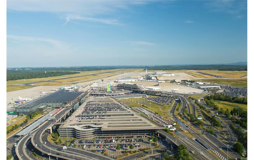 Luftaufnahme aus nordwestlicher Sicht auf den gesamten Komplex des Flughafens Köln/Bonn mit Parkdeck (mittig im Vordergrund), Terminal 2 (links) und daran anknüpfendem Terminal 1 (in der Mitte des Bildes)und sich dahinter befindlichen Start-und Landebahnen und dem "Cologne Bonn Cargo Center" (2013).