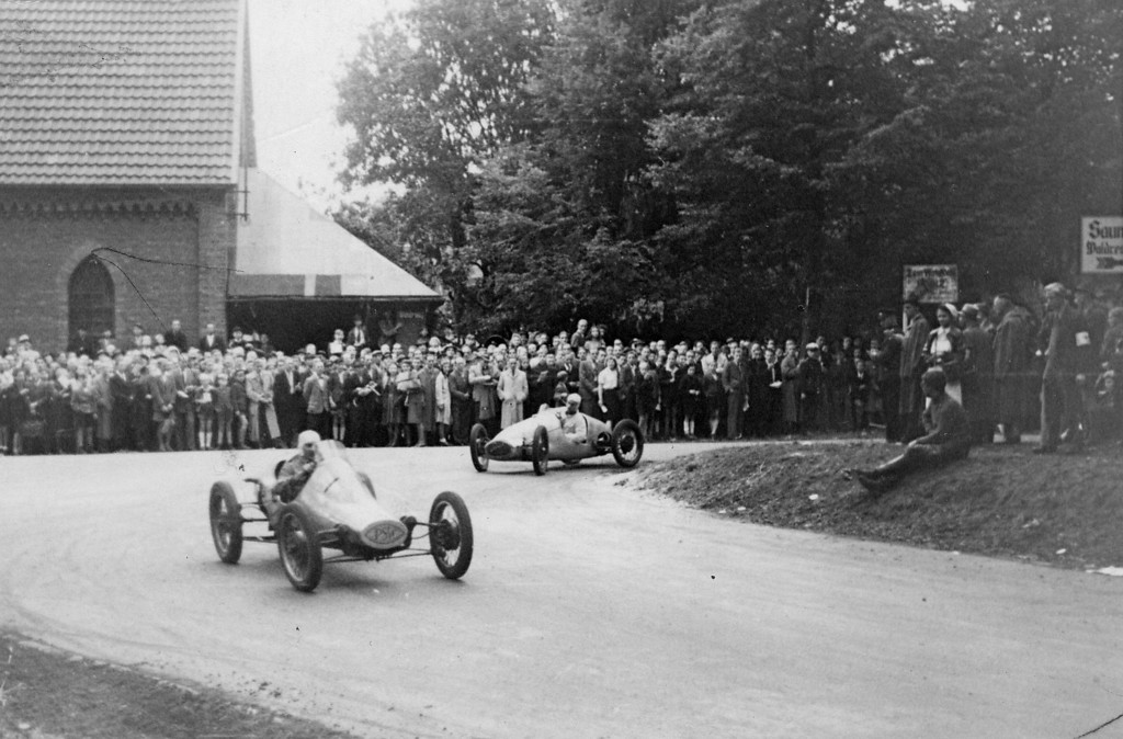 Bei dem am 12. September 1948 ausgetragenen Rennen "Um das Bayerkreuz" umfahren Kleinstrennwagen die scharfe Kurve an der Gezelinkapelle im heutigen Leverkusen-Alkenrath (links im Hintergrund).