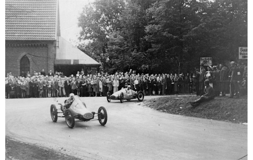 Bei dem am 12. September 1948 ausgetragenen Rennen "Um das Bayerkreuz" umfahren Kleinstrennwagen die scharfe Kurve an der Gezelinkapelle im heutigen Leverkusen-Alkenrath (links im Hintergrund).