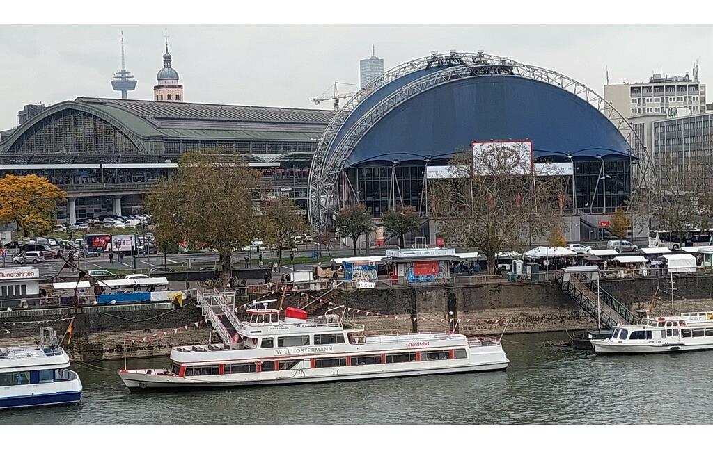 Das Kölner Rheinufer zwischen Trankgasse und Goldgasse: Das nach dem Kölner Volkssänger und Karnevalisten Wilhelm "Willi" Ostermann (1876-1936) benannte Personenfahrgastschiff auf dem Rhein, dahinter links der Kölner Hauptbahnhof und rechts der im Oktober 1996 eröffnete Musical Dome (2021).