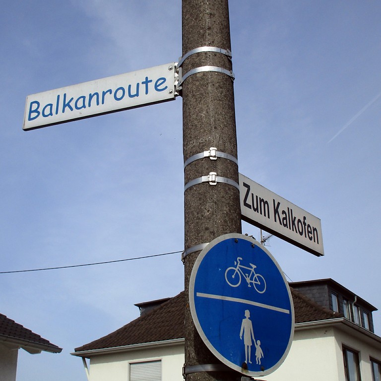 Die zumeist als "Rhabarberschlitten" bekannte Kleinbahn Siegburg - Zündorf wird an einem Schild an der Straße "Zum Kalkofen" in Troisdorf-Bergheim "Balkanroute" genannt (2017).