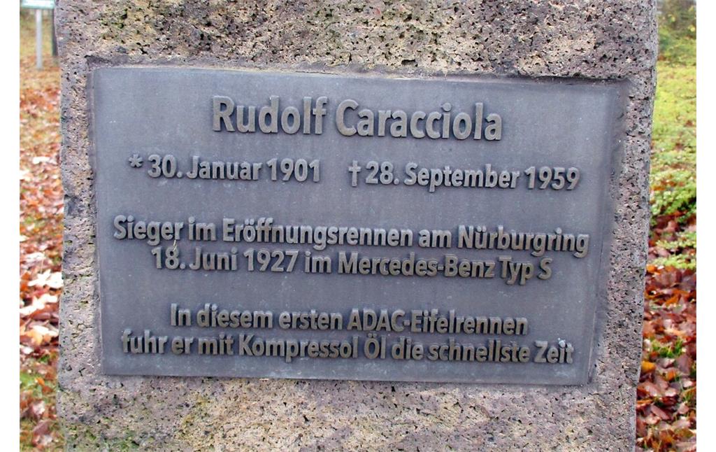 Die obere der beiden Inschriftentafeln an dem Denkmal für den Rennfahrer Rudolf Caracciola (1901-1959) am Nürburgring ehrt diesen als Sieger im Haupt-Eröffnungsrennen der Strecke, das allerdings entgegen der Inschrift am 19. Juni 1927 stattfand (2020).