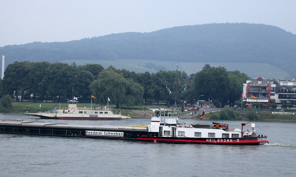 Die Rheinfähre "Konrad Adenauer" beim Ablegen auf der Niederdollendorfer Rheinseite (2018), davor ein kreuzendes Frachtschiff.