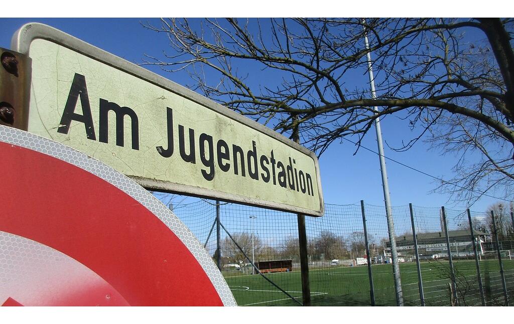 Straßenschild "Am Jugendstadion" in Düren-Rölsdorf, im Hintergrund die historische Sportanlage (2021).