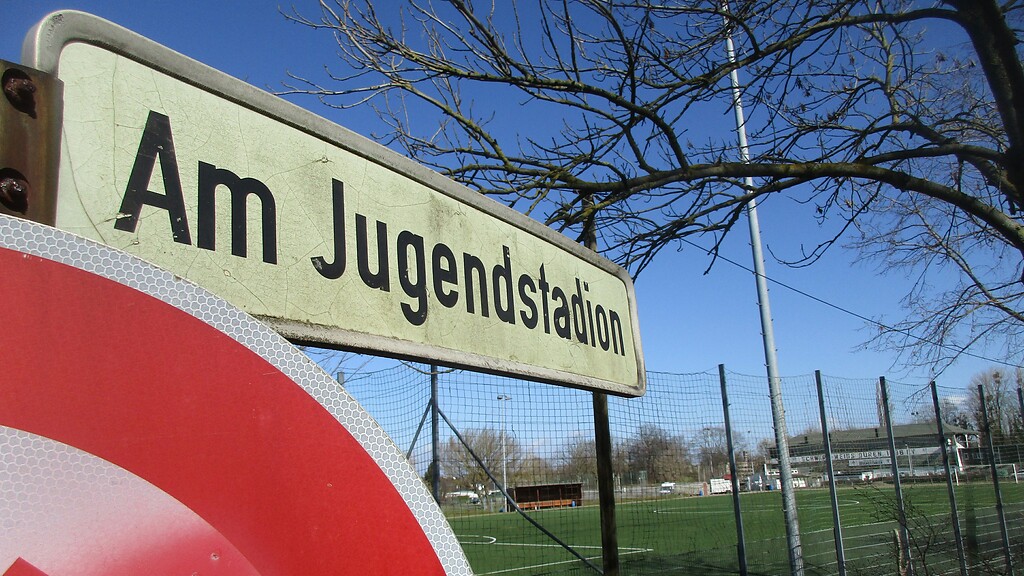 Straßenschild "Am Jugendstadion" in Düren-Rölsdorf, im Hintergrund die historische Sportanlage (2021).