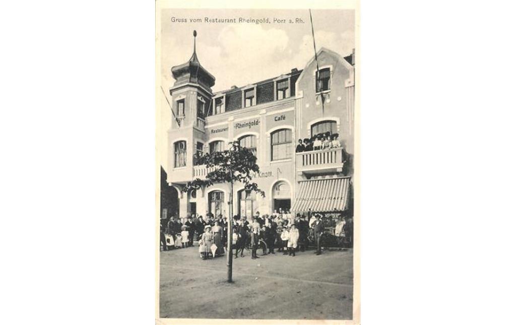 Historische Ansichtskarte von 1915 aus Porz mit der Aufschrift "Gruss vom Restaurant Rheingold, Porz a. Rh.". Das einstöckige Gasthaus Knott wurde um das Jahr 1910 aufwendig ausgebaut und als "Hotel Rheingold" eröffnet, dessen repräsentative Fassade zum heutigen Friedrich-Ebert-Ufer hin mit Turm und Balkonen ausgestattet war.