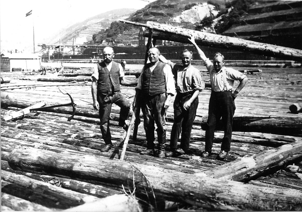 Vier Männer auf einem Rheinfloß, der zweite von links hält einen Lappen, eine seitliche Ruderstange (um 1910)