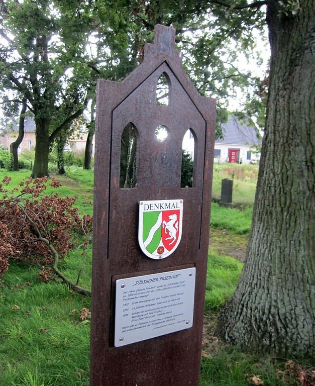 Eine metallene Stele mit der Denkmalplakette und einer Informationstafel auf dem jüdischen Friedhof in Hülchrath (2014).
