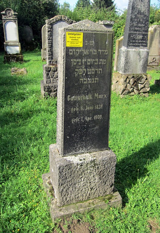 Grabsteine auf dem jüdischen Friedhof in Wevelinghoven. Im Vordergrund befindet sich ein Grabstein mit einem Hinweisschlid auf mangelnde Standfestigkeit (2014)
