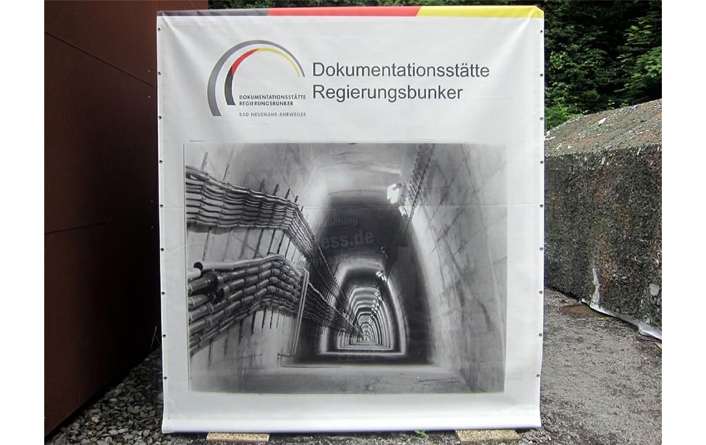 Im Eingangsbereich zur Dokumentationsstätte Regierungsbunker aufgespannte Informationsplane zu dem ehemaligen "Ausweichsitz der Verfassungsorgane des Bundes" bei Ahrweiler (2015). Das Foto auf der Plane zeigt den Blick in einen der Tunnel des früheren Bunkers, den Verbindungsstollen zwischen den Bauteilen Ost und West.