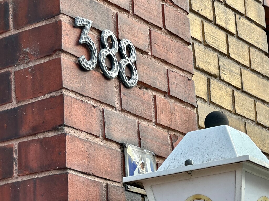 Die durchgestrichene Nummer 74 hinter der Laterne erinnert an die vormalige Zählung der Hausnummern entlang der Hauptstraße in Köln-Porz. Diese begann bis in die 1960er Jahre erst an der Ortsgrenze zu Zündorf (2023).