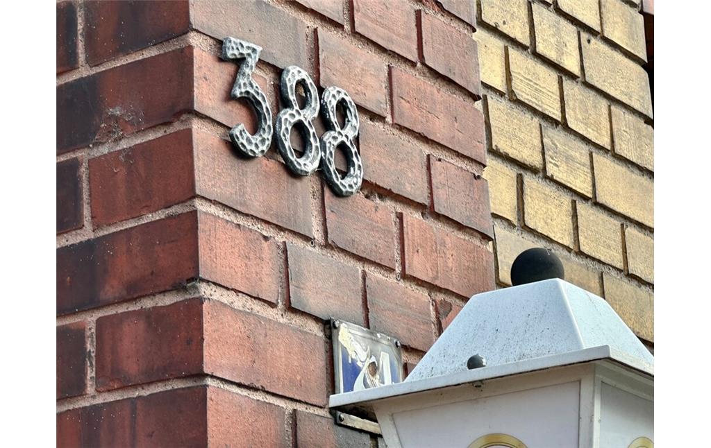 Die durchgestrichene Nummer 74 hinter der Laterne erinnert an die vormalige Zählung der Hausnummern entlang der Hauptstraße in Köln-Porz. Diese begann bis in die 1960er Jahre erst an der Ortsgrenze zu Zündorf (2023).