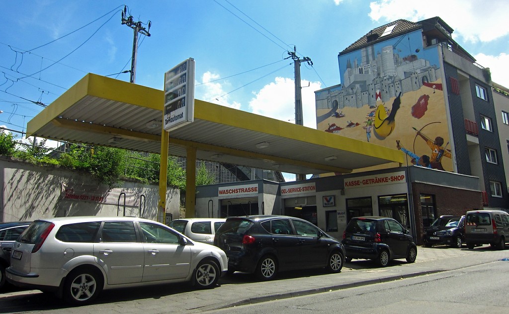 Die ehemalige Tankstelle in der Kölner Marzellenstraße, die heute als KFZ-Service und Waschanlage betrieben wird (2015). Die Fassade des Hauses dahinter ist durch ein großformatiges Graffiti gestaltet.