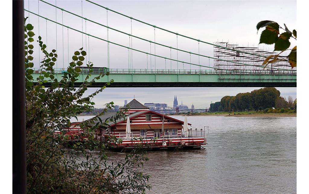 Blick in Richtung des Kölner Doms und die Rodenkirchener Autobahnbrücke in Köln-Rodenkirchen (2021). Im Vordergrund auf dem Wasser ist das Lokal "Alte Liebe" zu sehen.