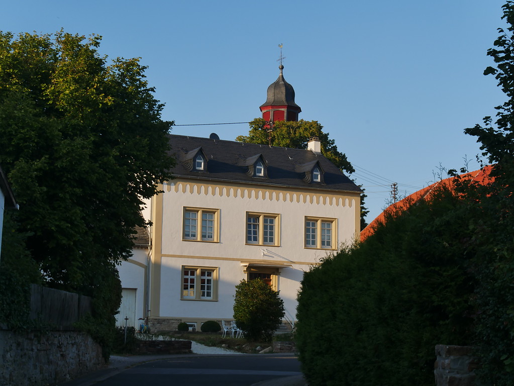 Südliche Ansicht des alten Pfarrhauses in Dörrebach mit dem Turm der katholischen Kirche (2016)