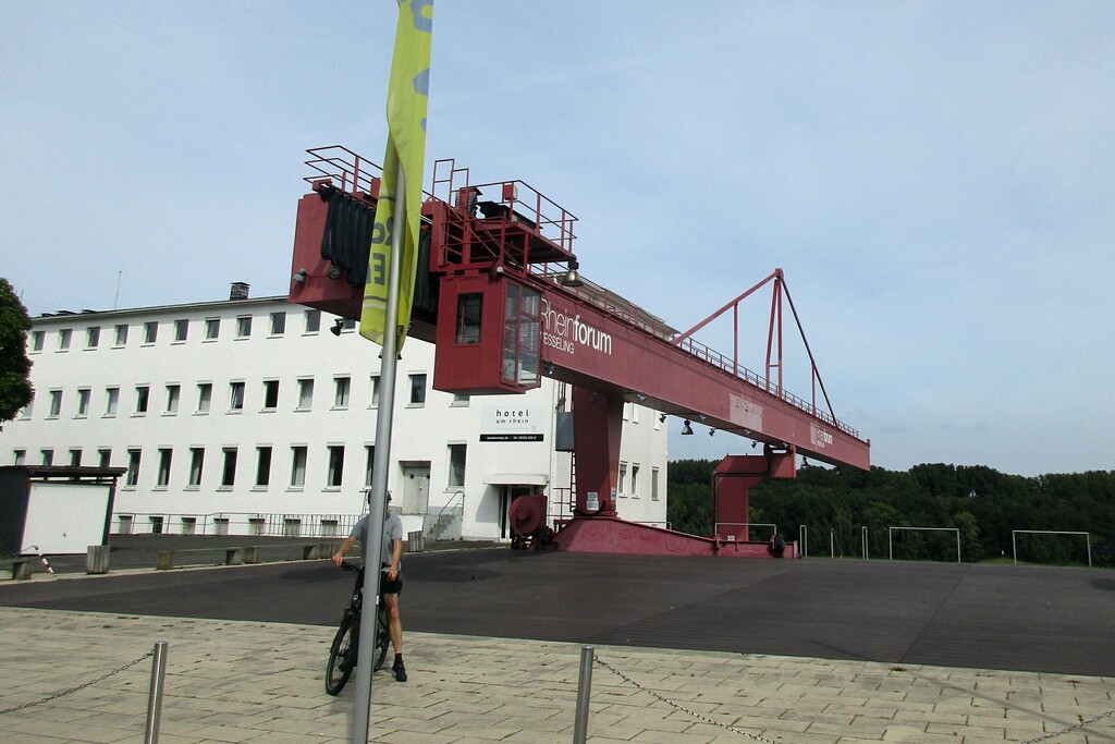 Historischer Hafenkran am Platz-am-Rheinforum in Wesseling, dahinter ein Gebäude des "Hotel am Rhein" (2023).