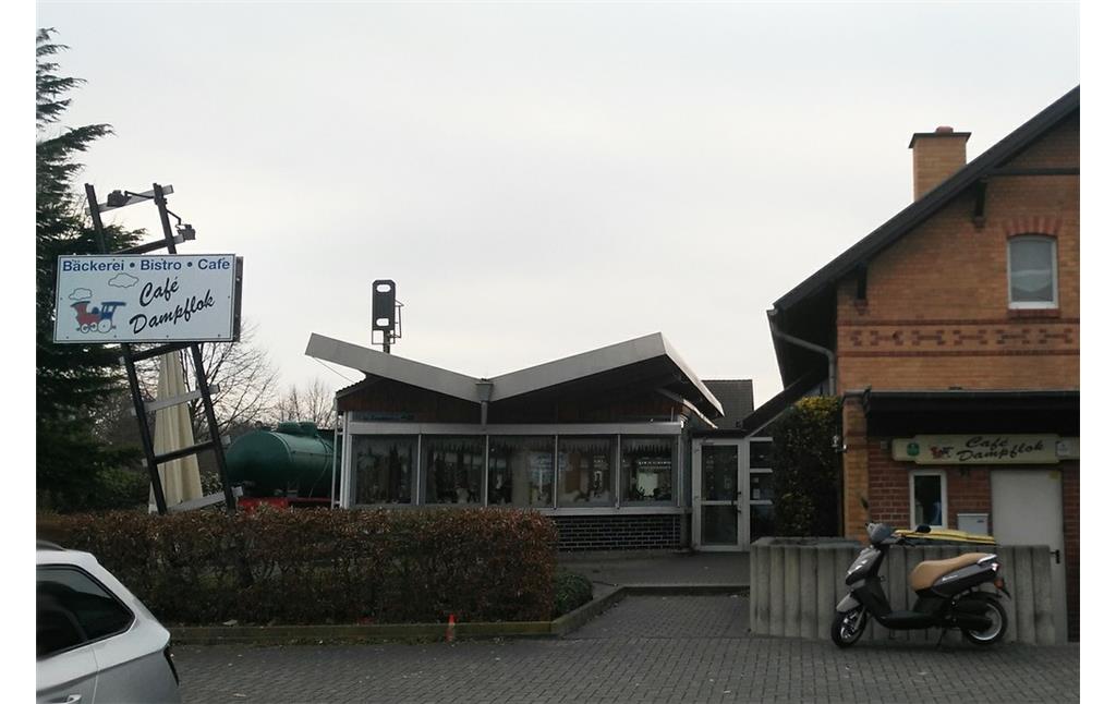 Café Dampflok im umgebauten Bahnhofsgebäude des ehemaligen Kleinbahnhof Ost in Elsdorf (2018), links das Schild zum Café auf einer Schiene, dahinter die alte Dampfspeicherlok.