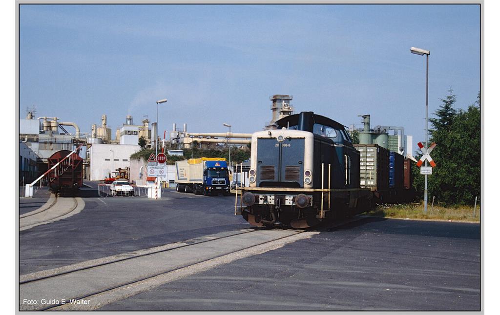 Ein Güterzug mit einer Diesellokotive des Typs der DB-Baureihe V 100 / 211 bei der Einfahrt in die Spanplattenfabrik der Glunz AG in Kaisersesch über das Industriestammgleis vor Ort (1992).
