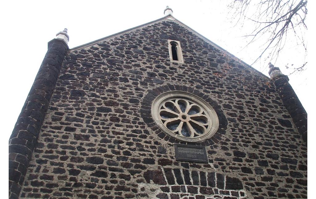 Der obere Bereich der Fassade der Synagoge in der Ostergasse in Polch mit dem Tuffsteinradfenster und darüber dem schlitzartigen maurischen Fenster (2022).
